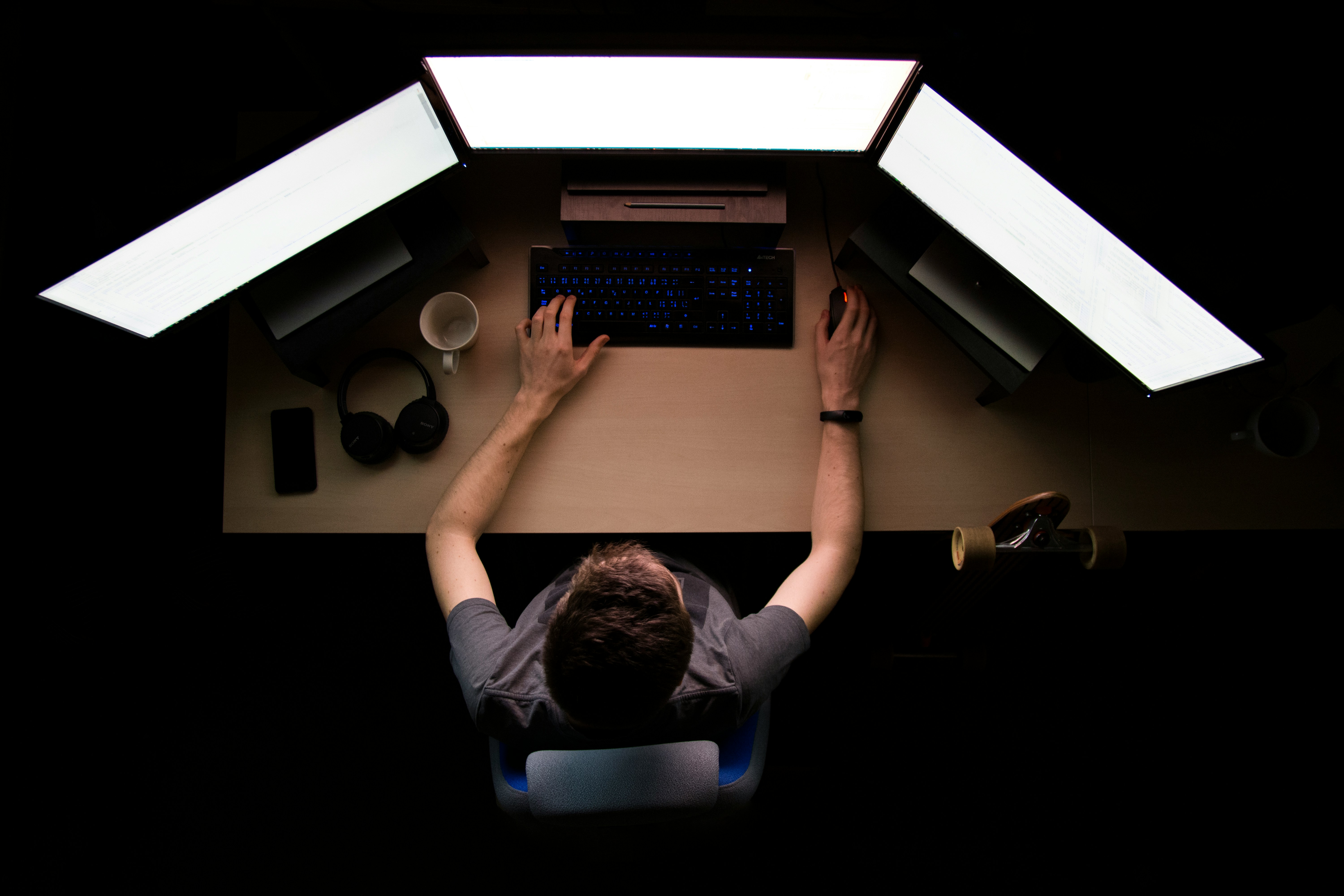 Overhead view of an analyst working across three monitors in a dark room